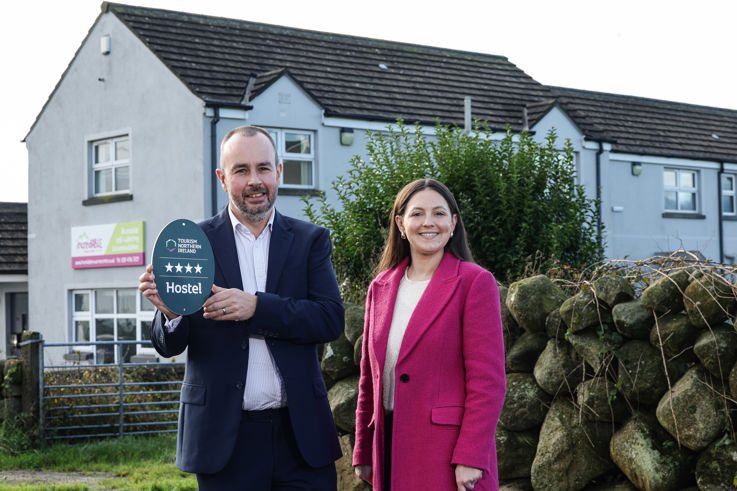 A man and woman pose in front of a house, each holding a plaque between them.